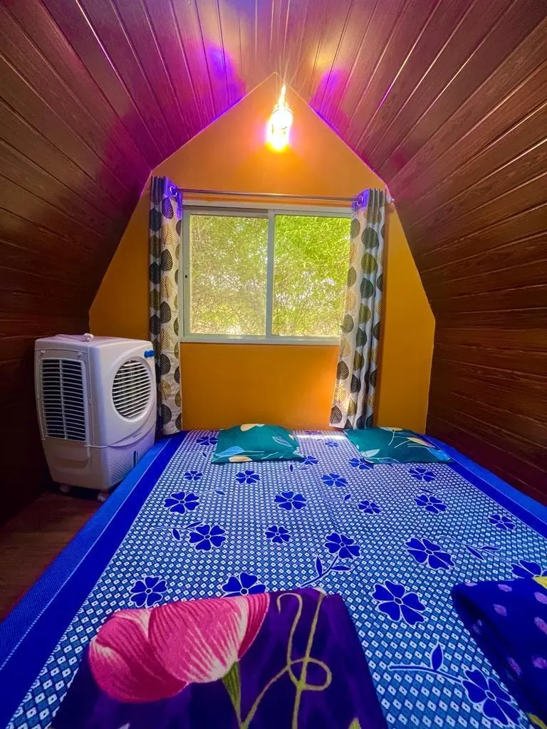 Inside a Pawna Machi cottage with a bed and air cooler